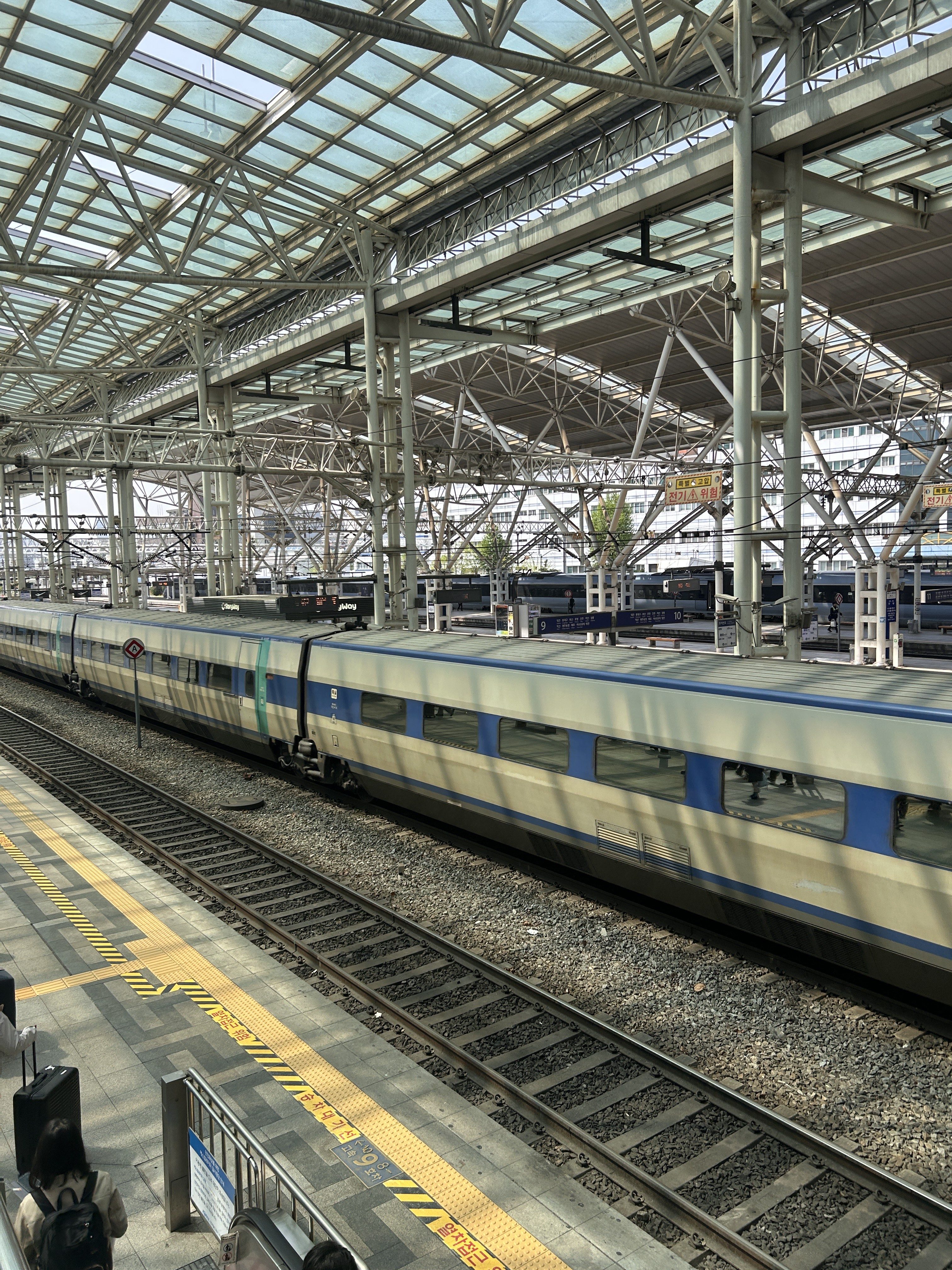 A view of a modern train station with a sleek train parked on the tracks, partially visible behind a platform edge.