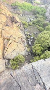 A rocky landscape featuring large boulders and patches of green shrubbery. 
