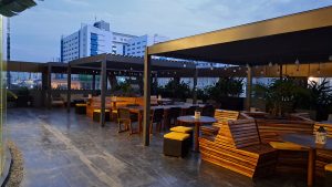 A rooftop terrace with wooden furniture arranged in clusters, including benches and tables.