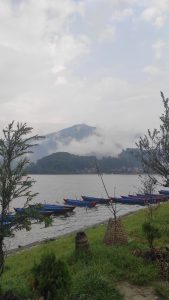 Blue and red canoes lined up on the shore of a lake with mountains in the background. Clouds in the sky create an overcast and dark atmosphere.