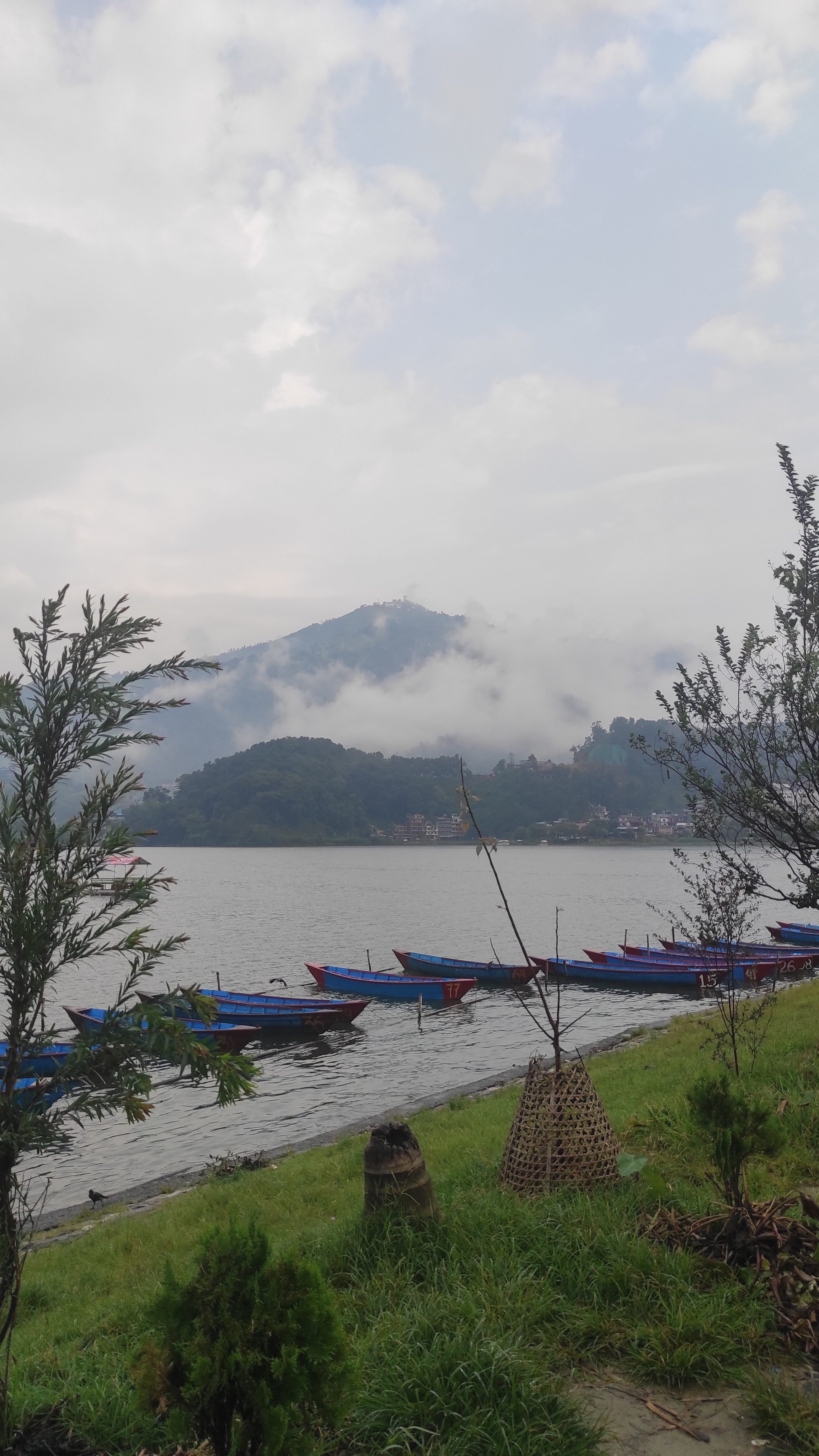 Blue and red canoes lined up on the shore of a lake with mountains in the background. Clouds in the sky create an overcast and dark atmosphere.