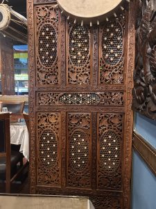 An intricately carved wooden screen with decorative patterns featuring oval shapes and floral motifs, allowing light to filter through.