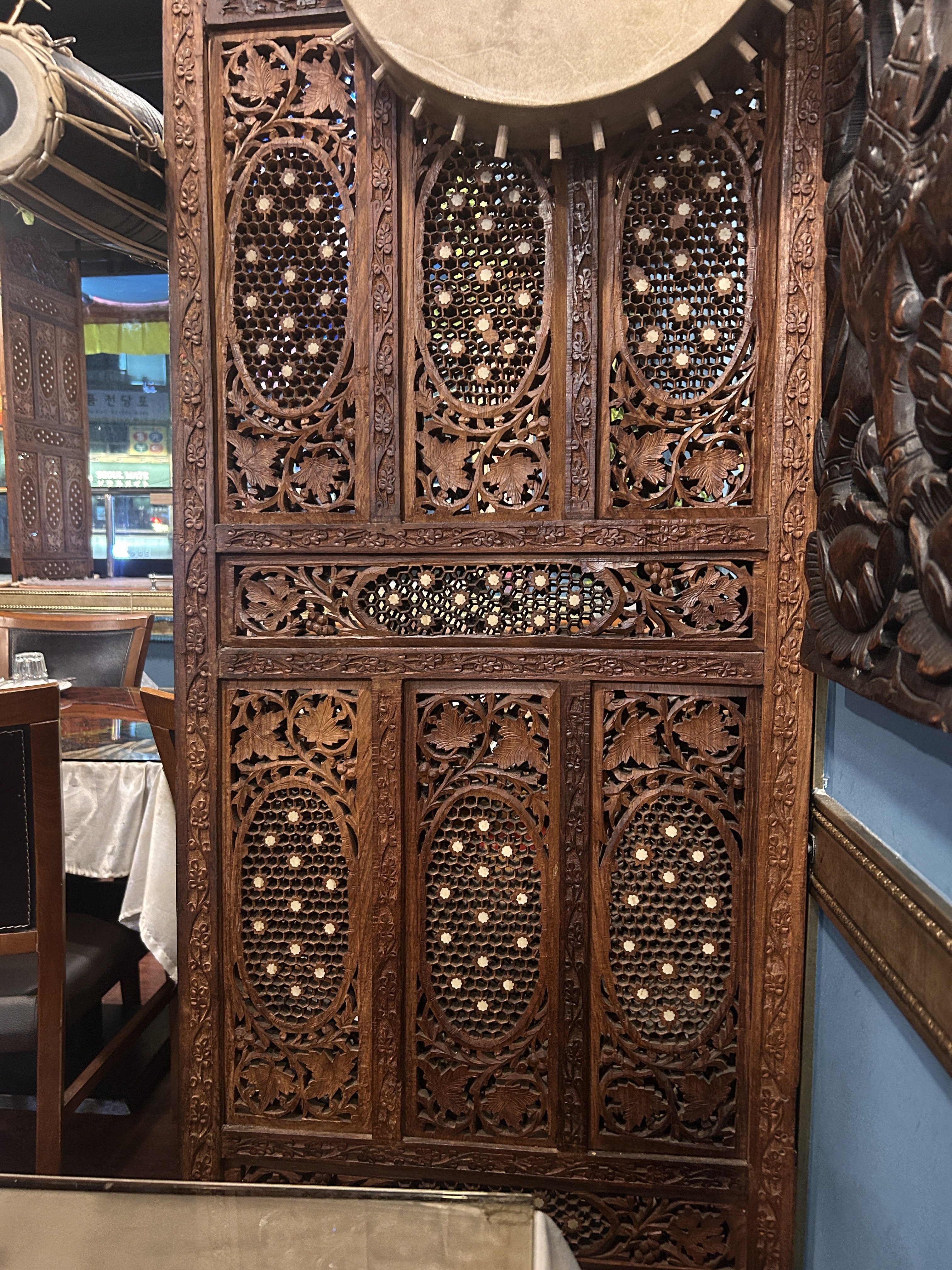 An intricately carved wooden screen with decorative patterns featuring oval shapes and floral motifs, allowing light to filter through.