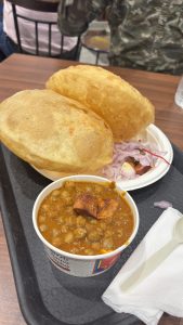 A plate of Indian cuisine Chole Bhature featuring two large, golden puris served alongside a bowl of chana masala, a spicy chickpea dish.
