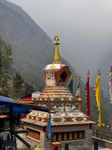 A beautifully adorned stupa featuring intricate decorations and a golden spire stands prominently in a mountainous landscape. 