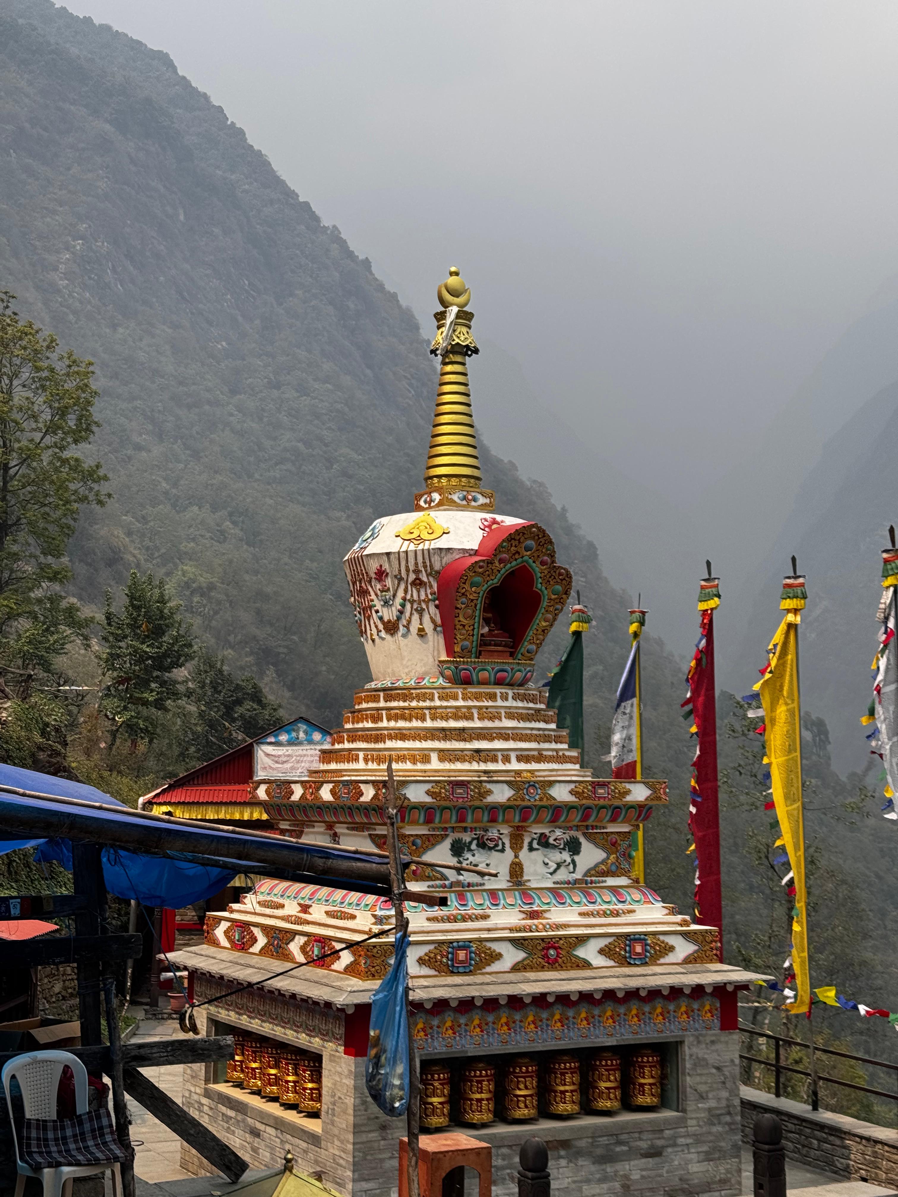 A beautifully adorned stupa featuring intricate decorations and a golden spire stands prominently in a mountainous landscape.