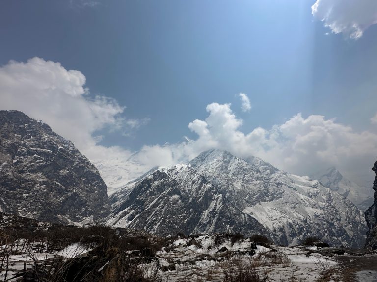 A panoramic view of snow-capped mountains under a partly cloudy sky.