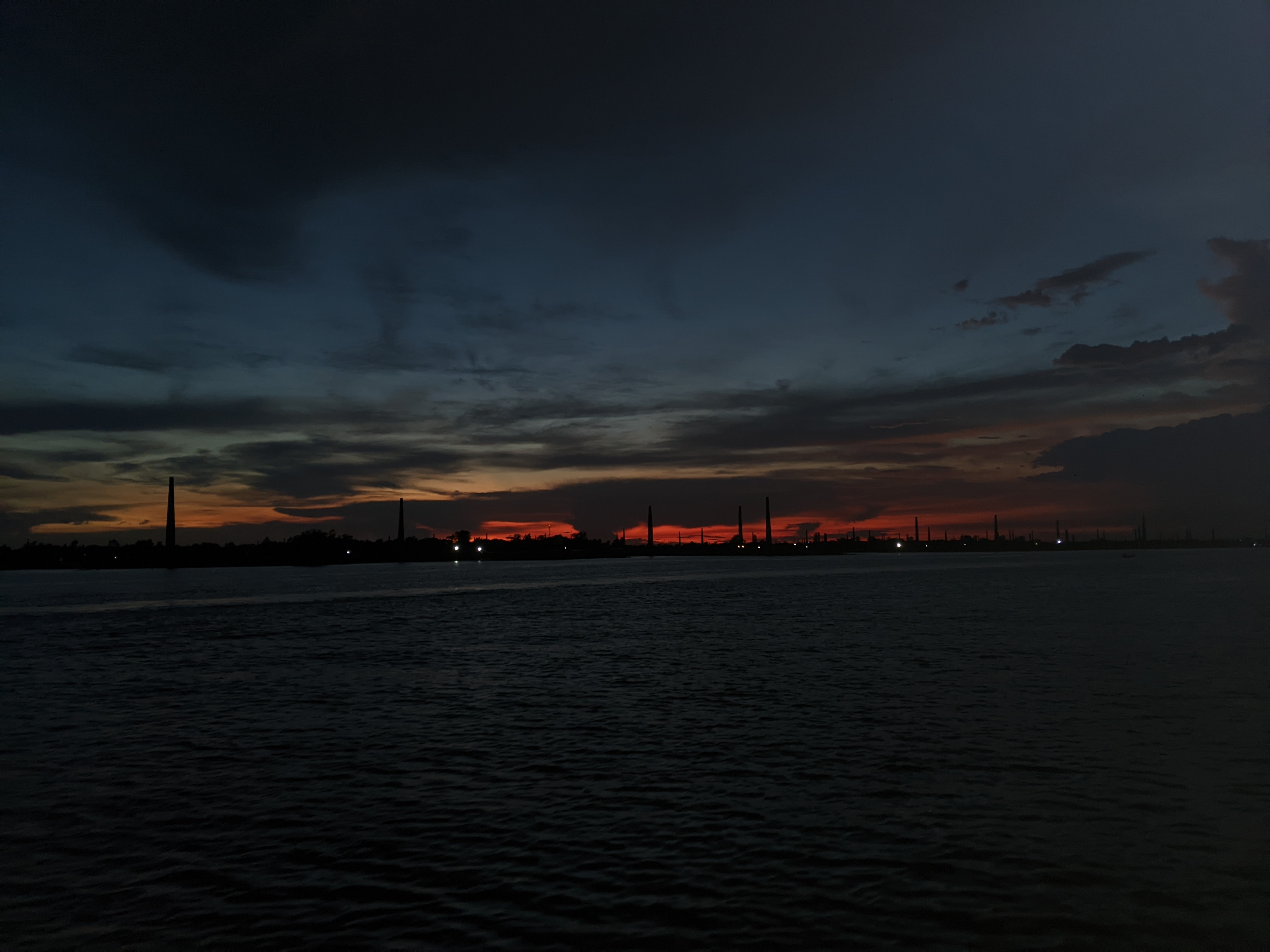 A scenic twilight view over a body of water, showcasing a gradient sky transitioning from dark blue to a warm orange and red near the horizon.