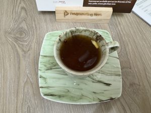 A cup of tea with a lemon slice on a green marbled plate.
