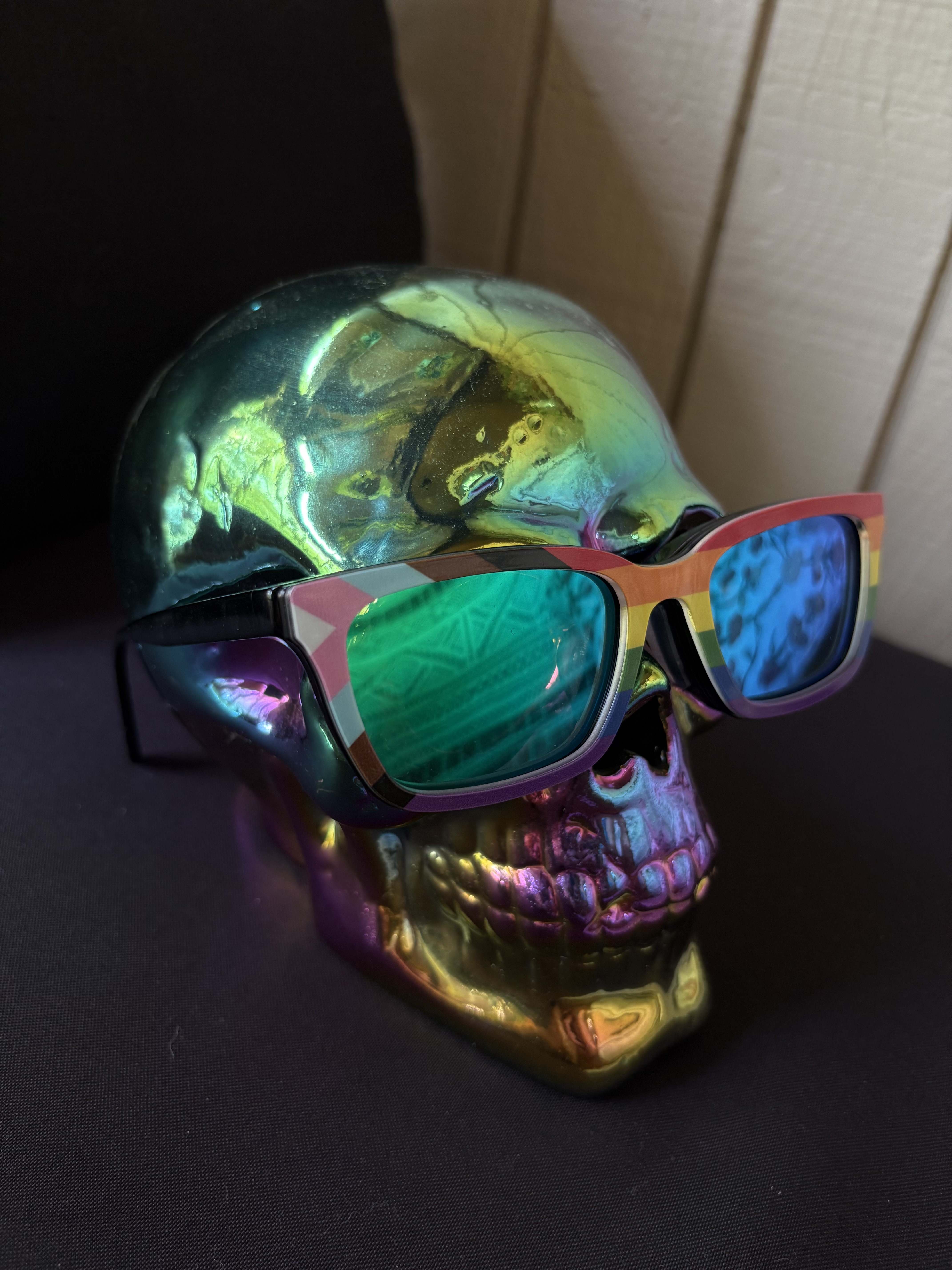 Iridescent green and purple mirrored skull wearing reflective sunglasses with progress pride flag rims.