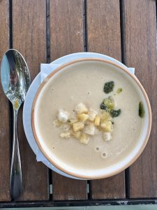 A creamy soup garnished with golden croutons and a drizzle of green herb oil is served in a ceramic bowl on a wooden table.