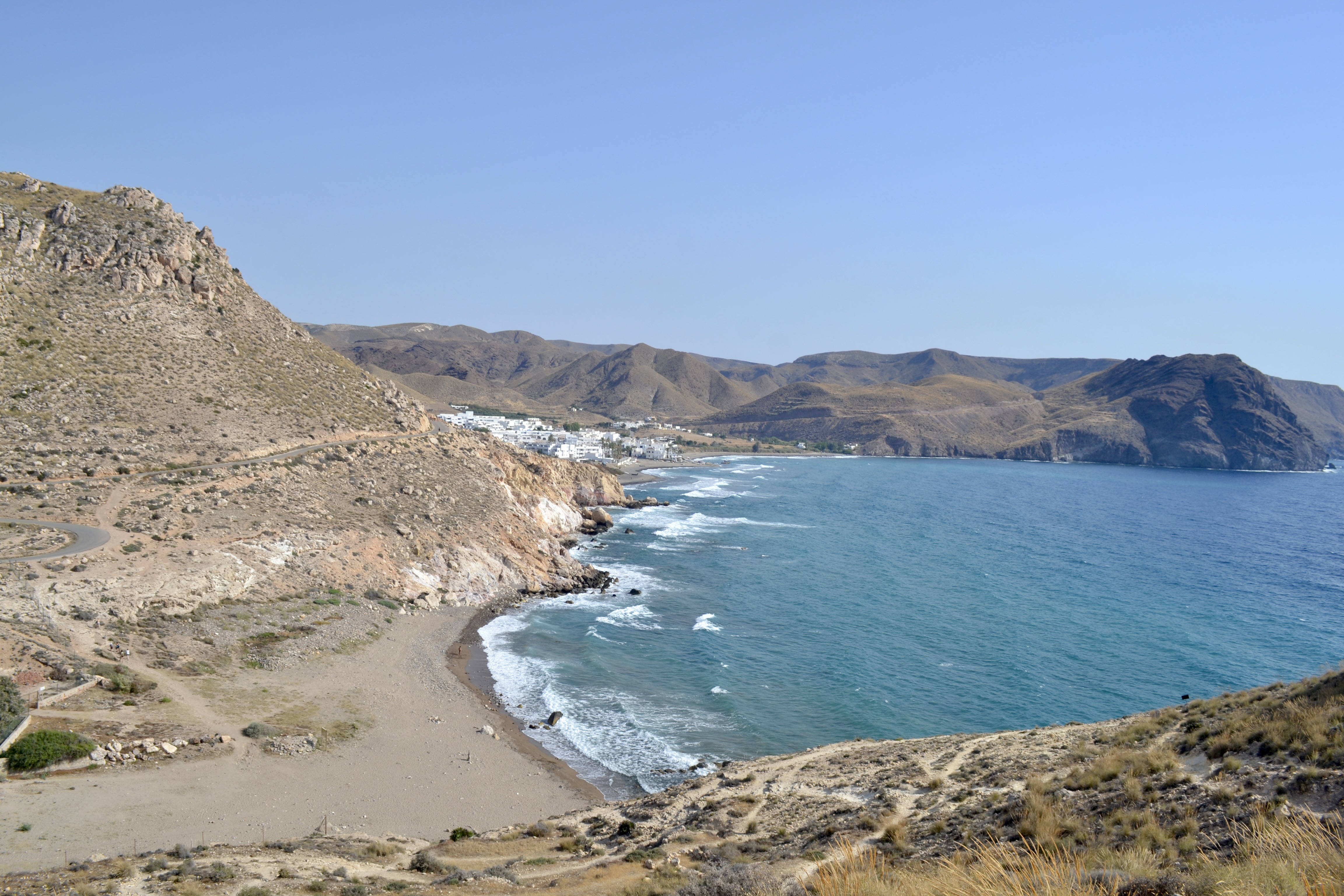 A scenic coastal view in Almería, Spain, with rocky hills descending to a calm bay and a white village by the shore.