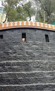 A close-up view of a textured black stone wall with a curved top.