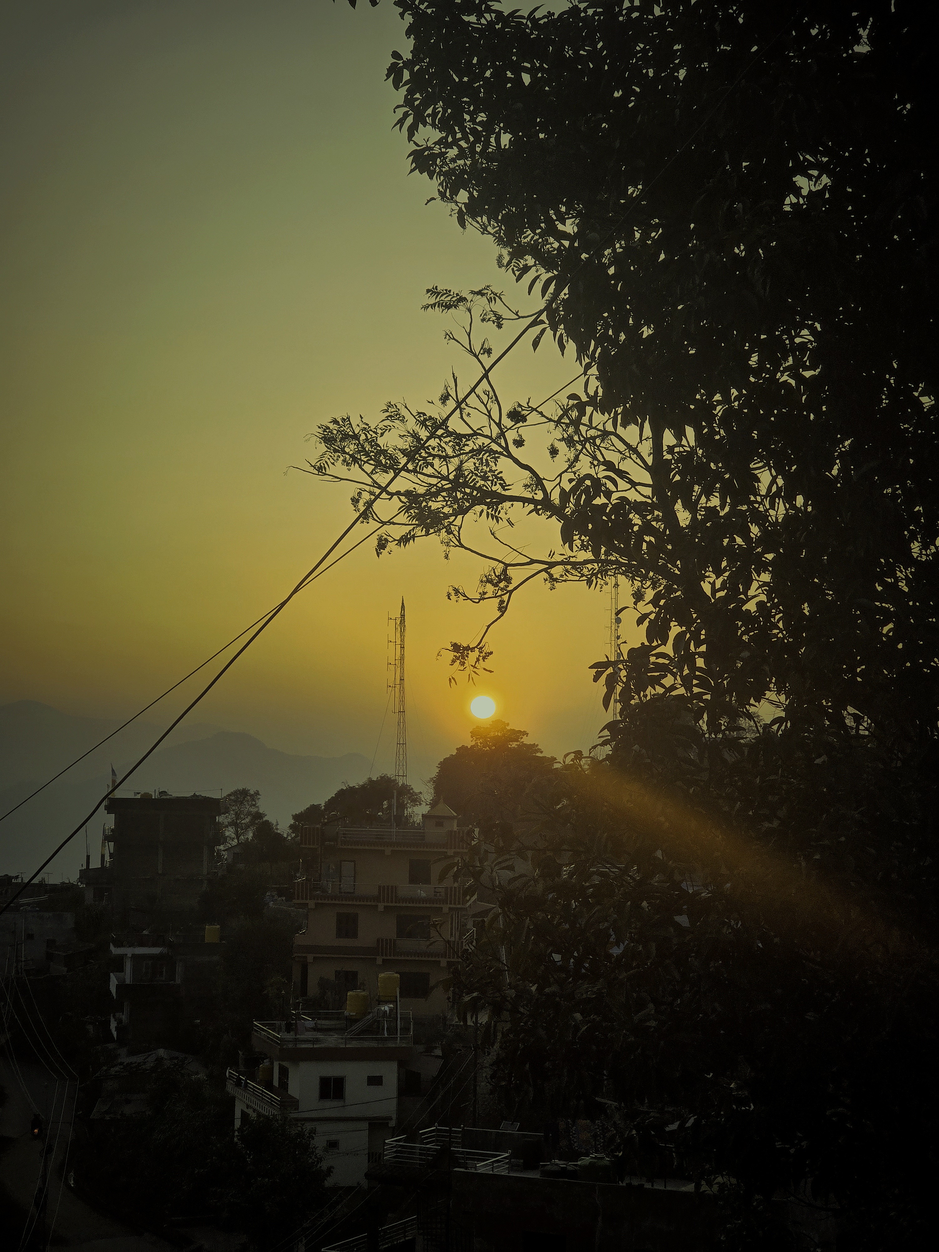 A serene sunset scene featuring a golden sun descending behind distant mountains, casting warm hues across the sky.