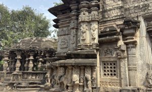 Side view of a carved stone temple with deity and animal sculptures. Elephant figures support divine statues above a lattice window with geometric patterns.