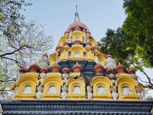 Low-angle view of Parvati Hill Temple in Pune, India, featuring a yellow-pink multi-tiered structure with intricate carvings and a small spire.