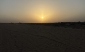 

Serene desert Sunrise with sun dipping below horizon in the distance.