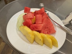 A plate of assorted fresh fruit, featuring slices of watermelon, pineapple, and a piece of honeydew melon, arranged neatly on a white plate.