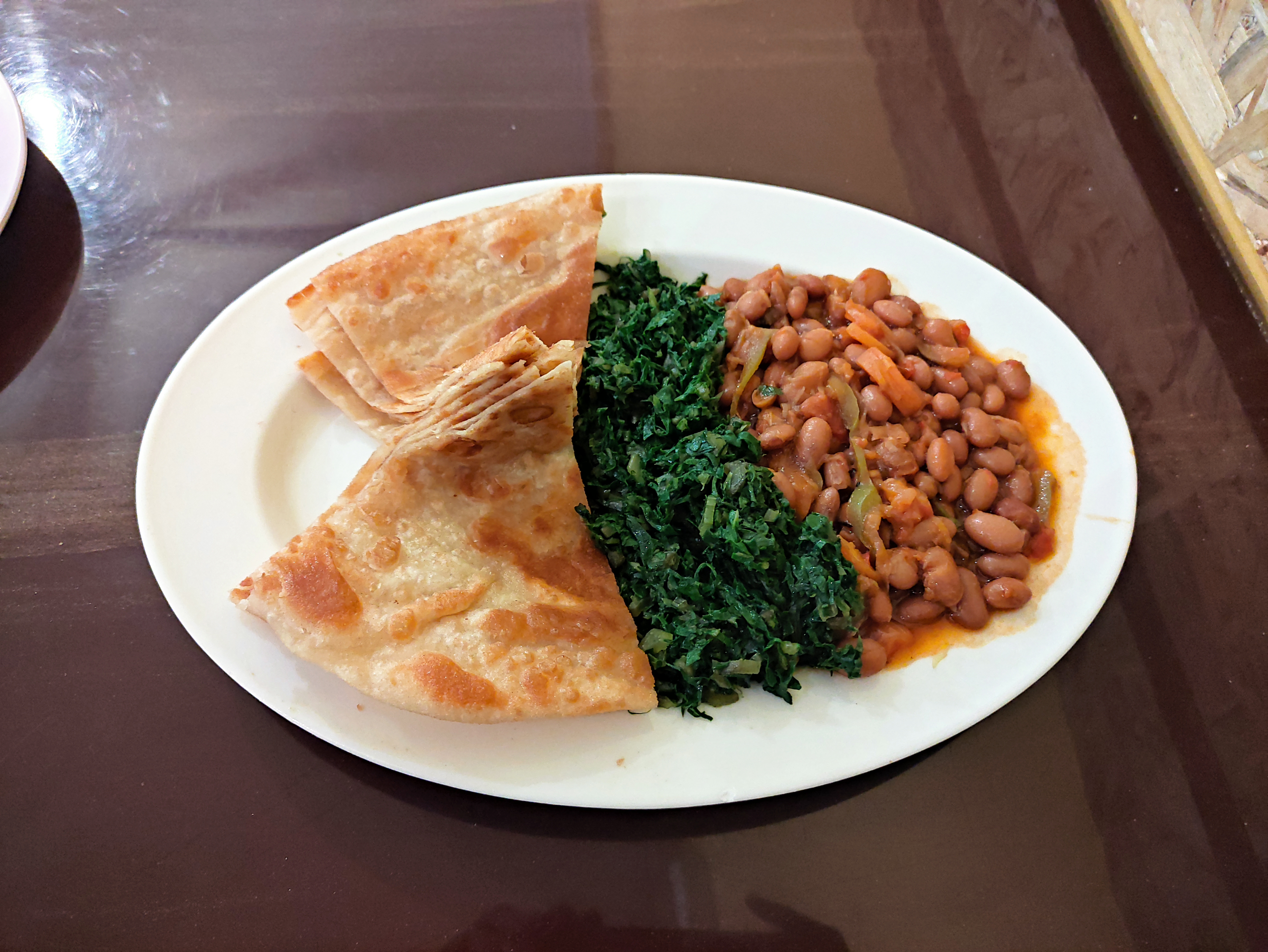 A delicious plate of Kenyan chapati, savory beans, and sautéed greens, beautifully arranged on a white plate.