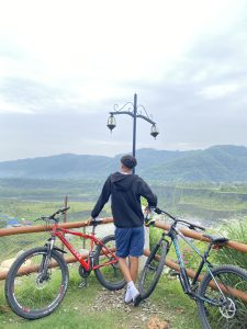 A person stands with their back to the camera, gazing at a scenic view of hills and valleys. 