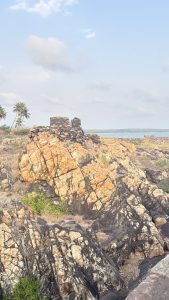 The image features a rocky coastline with large, colorful rock formations in shades of orange, black, and cream.