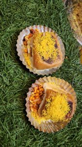 Two savory snacks are placed on decorative silver plates resting on green grass. 
