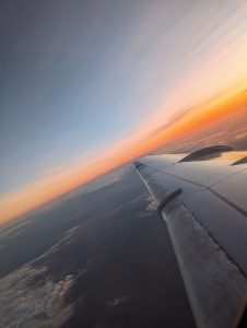A tilted-angle view of an airplane wing from the window, flying high above the clouds during a vibrant sunset.