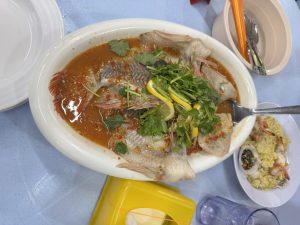 A plate of steamed fish in spicy sauce with lemon slices and herbs.
