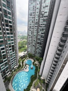 A view from above capturing a modern urban landscape featuring two tall residential buildings flanking a beautifully designed swimming pool.

