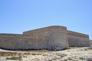 The historic Castillo de San Felipe, a coastal fortress in Los Escullos, Almería, Spain. It has strong stone walls with battlements and stands under a clear blue sky.