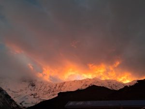 A stunning sunset at Tilicho Base Camp, where a mountain range glows under dramatic orange and yellow clouds.