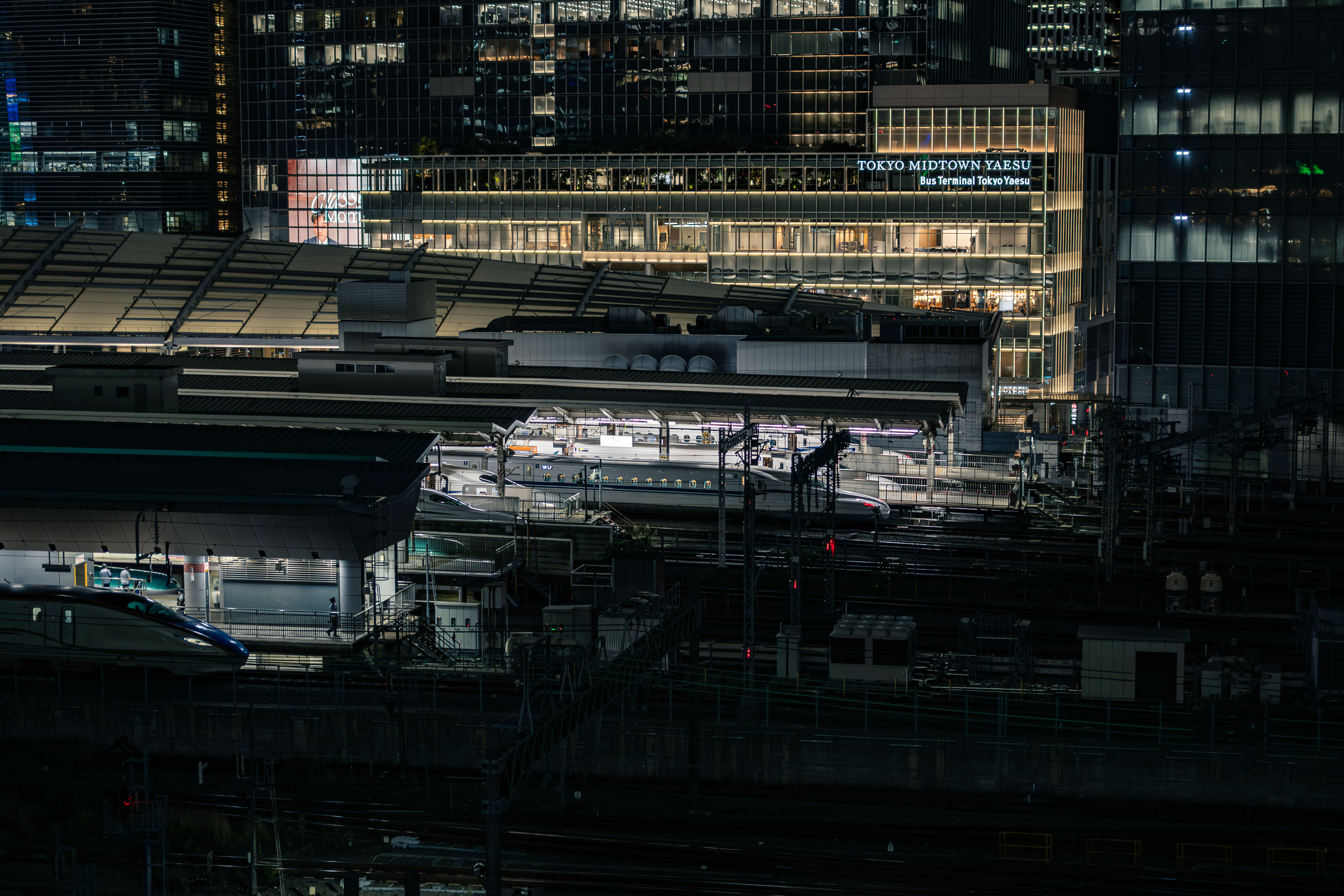 The brightly lit night view of Tokyo Midtown Yaesu. Right in front of it is Tokyo Station, where several Shinkansen trains are parked.
