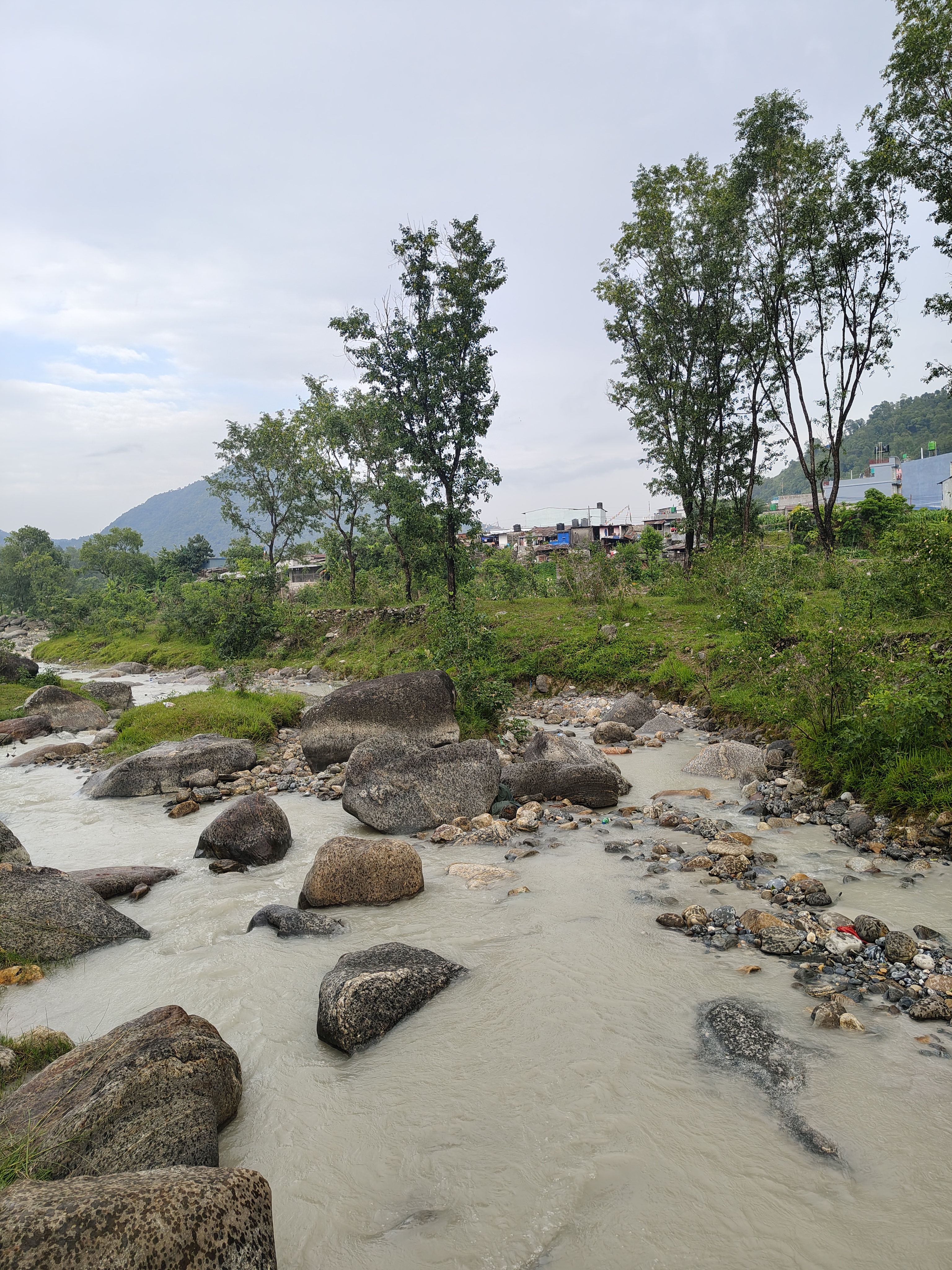 A serene view of a river winding through a rocky landscape, with large boulders scattered among smaller stones in the water.