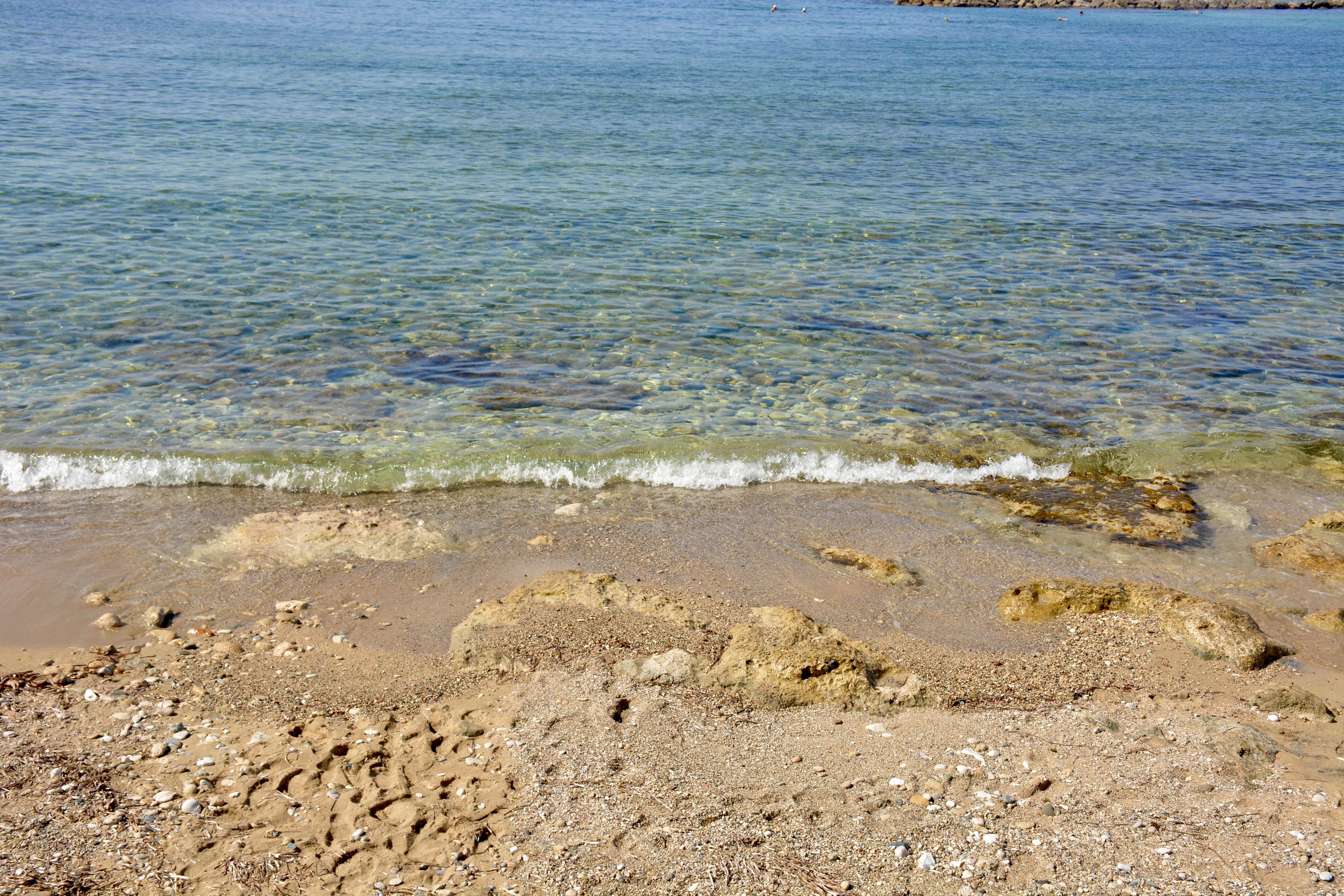 A serene beach in Paphos, Cyprus, with turquoise water lapping a sandy shore dotted with pebbles.