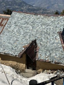 A close-up view of a sloped roof made of slate shingles, displaying various shades of blue and grey. 