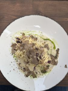 A luxurious plate of tagliolini pasta served in a creamy truffle sauce, generously topped with freshly shaved truffles and garnished with microgreens and a drizzle of herb oil.