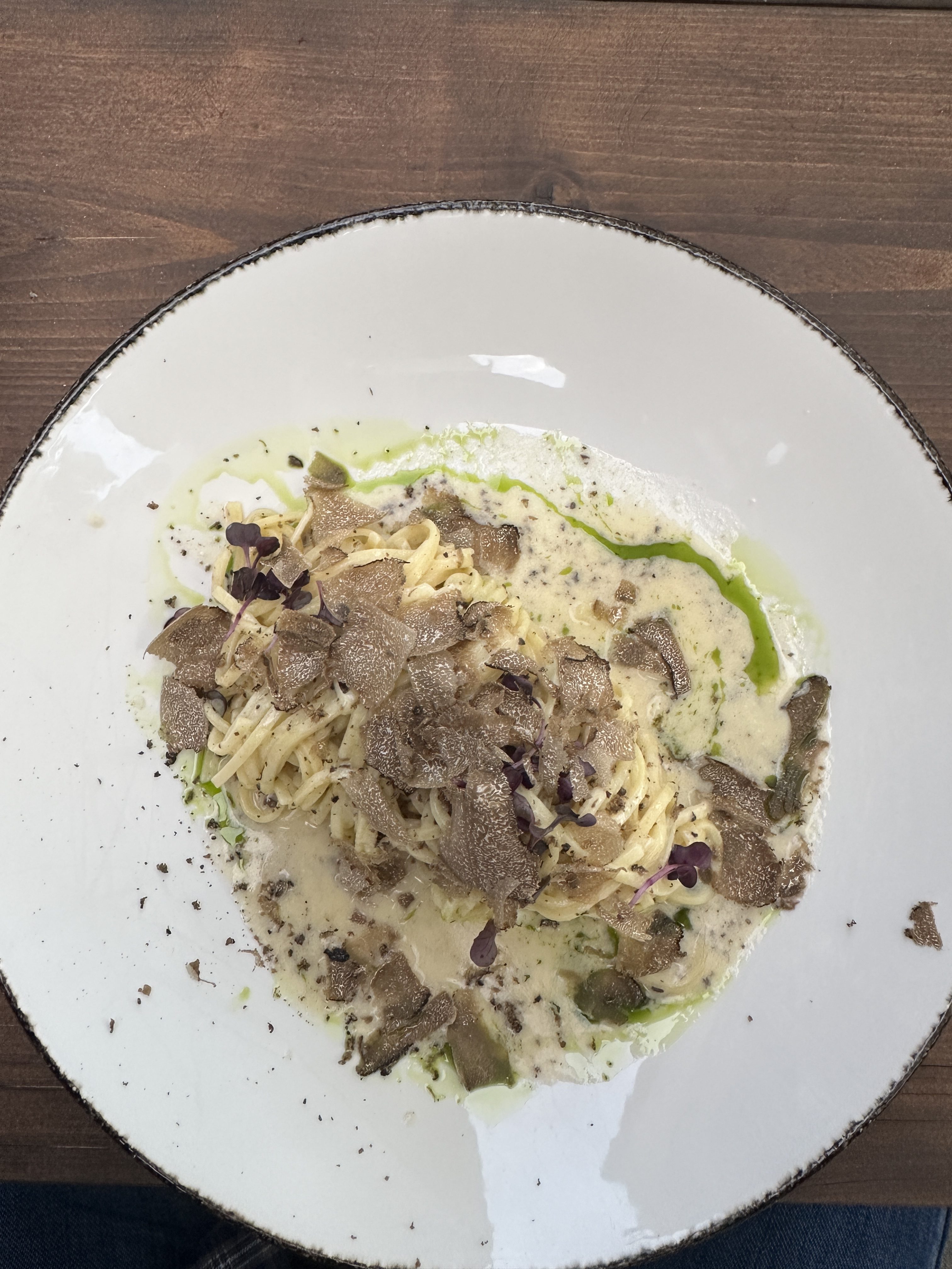 A luxurious plate of tagliolini pasta served in a creamy truffle sauce, generously topped with freshly shaved truffles and garnished with microgreens and a drizzle of herb oil.