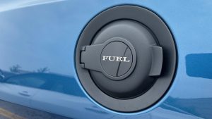 A fuel cap on the side of a blue car, with the word "FUEL" on it.