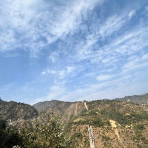 A scenic view of mountainous terrain under a clear blue sky, with wispy clouds scattered across the horizon. 