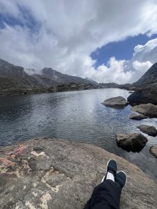 A wide view of a tranquil mountain lake surrounded by rocky terrain and steep mountains under a cloudy sky.