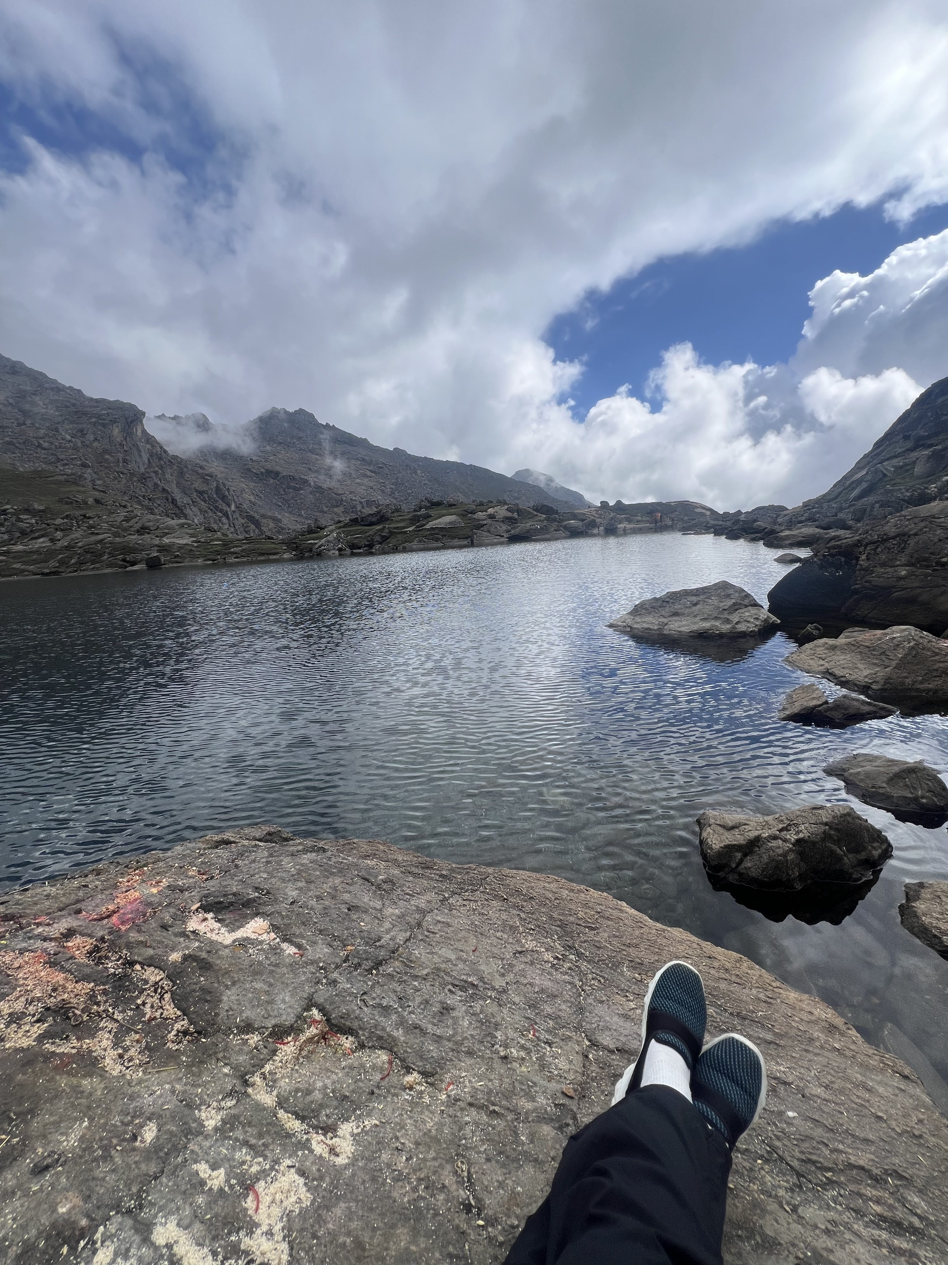 A wide view of a tranquil mountain lake surrounded by rocky terrain and steep mountains under a cloudy sky.