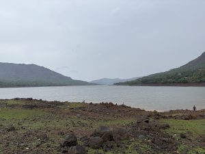 A lake, surrounded by mid-sized mountains on one side and land on the other, experiencing rainy weather