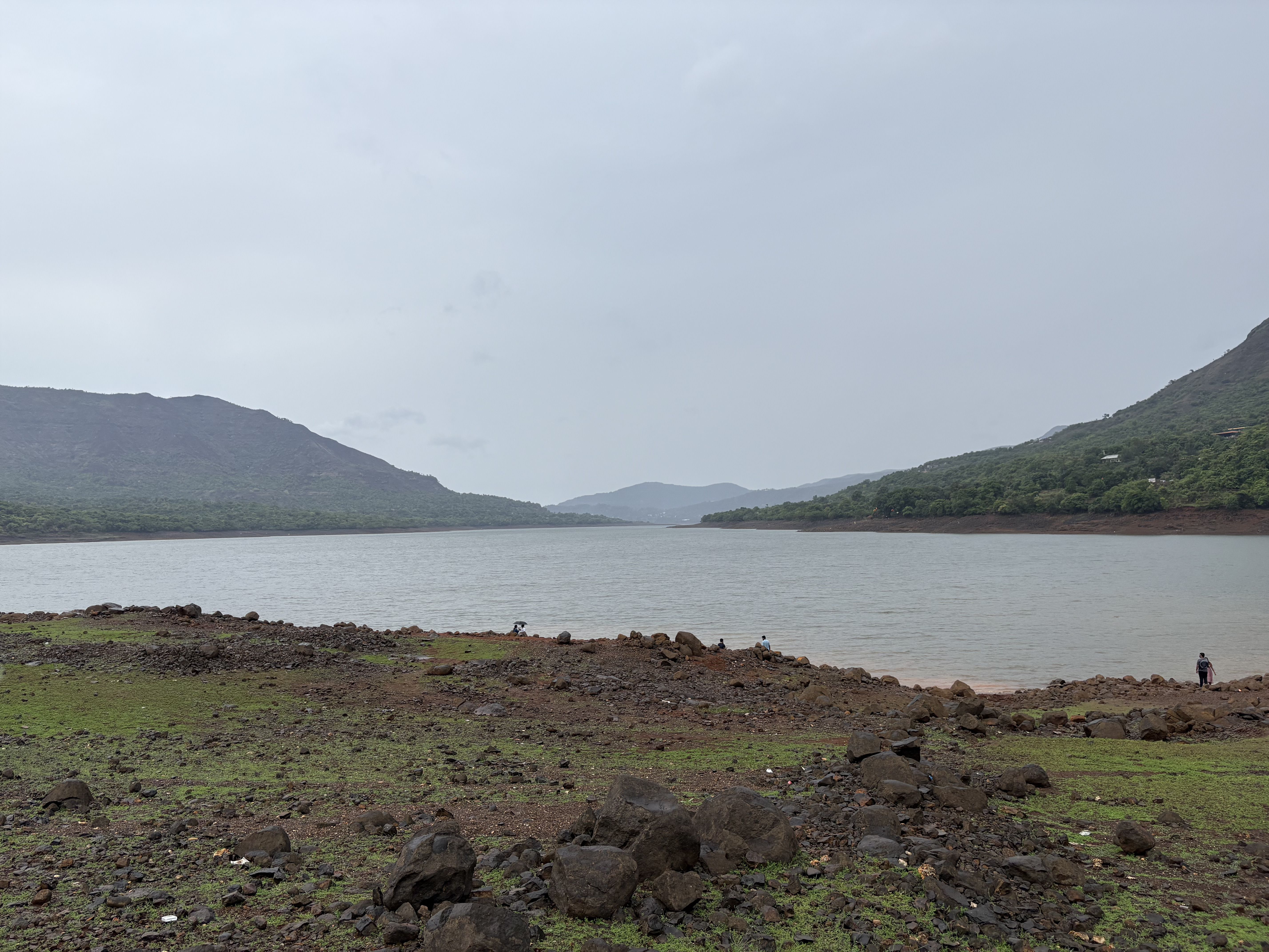 A lake, surrounded by mid-sized mountains on one side and land on the other, experiencing rainy weather