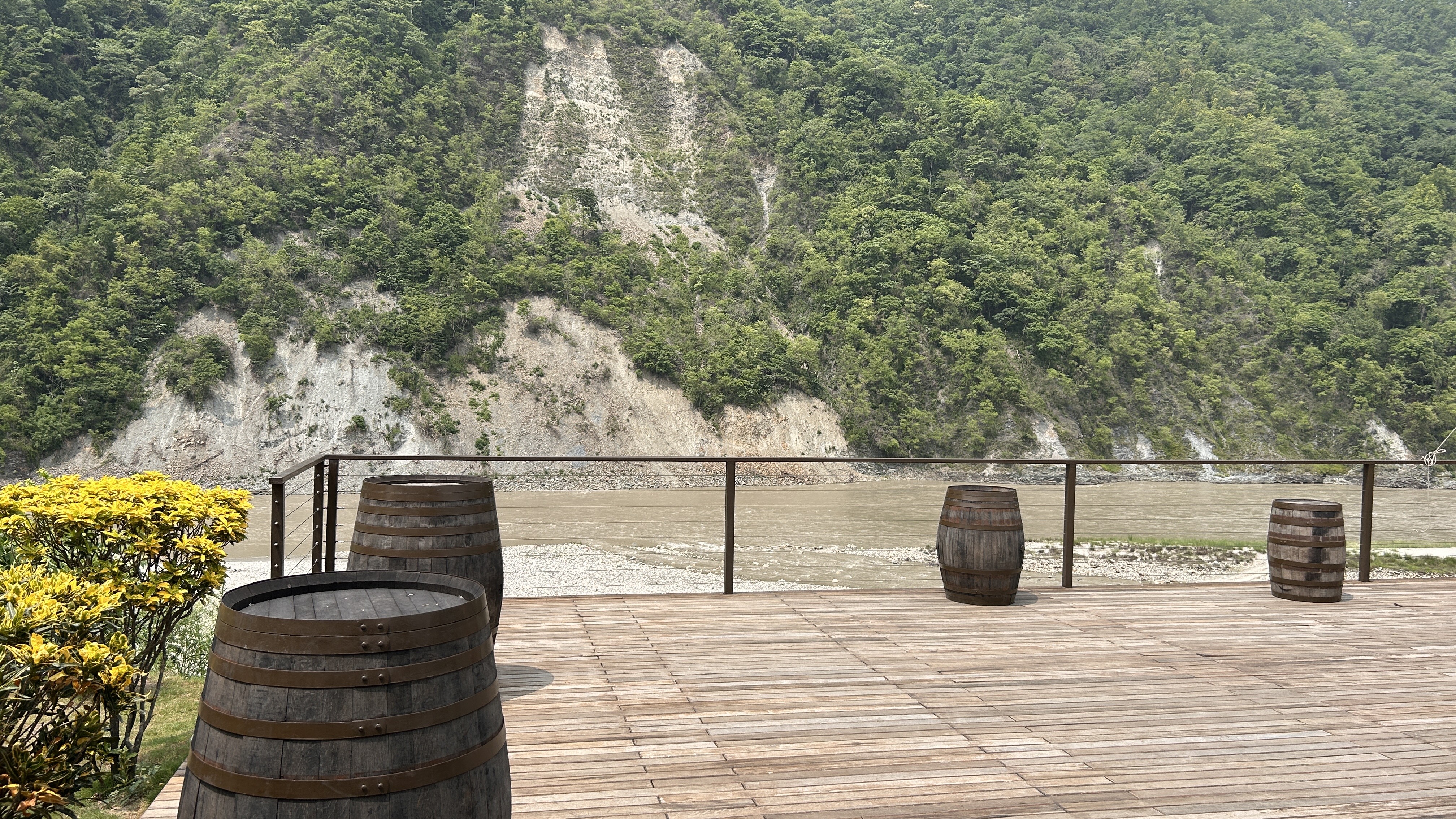 A wooden deck overlooks a river, surrounded by lush green hills and steep cliffs in the background.