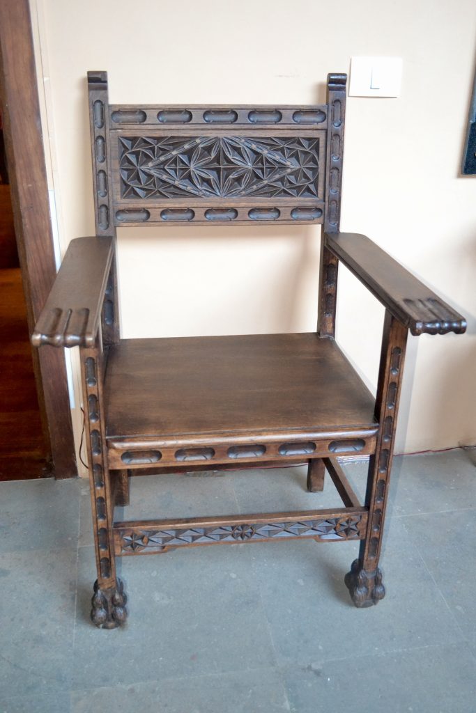 A 19th-century Spanish Colonial altar chair with intricate carvings and a wooden seat, photographed in Tenerife, Spain.