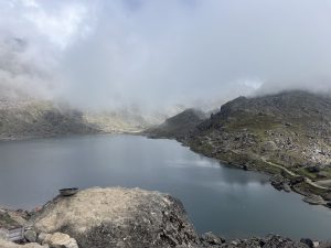 A serene mountain landscape featuring a tranquil lake surrounded by rocky slopes and a partially cloudy sky. 