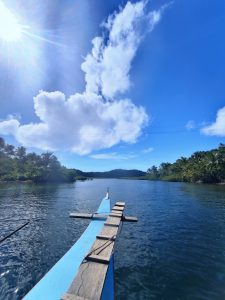A bright sunny day on a traditional wooden boat cruising through the calm waters of Siargao, Philippines. Surrounded by lush greenery and palm trees, with blue skies and dramatic clouds overhead, this image captures tropical island tranquility.