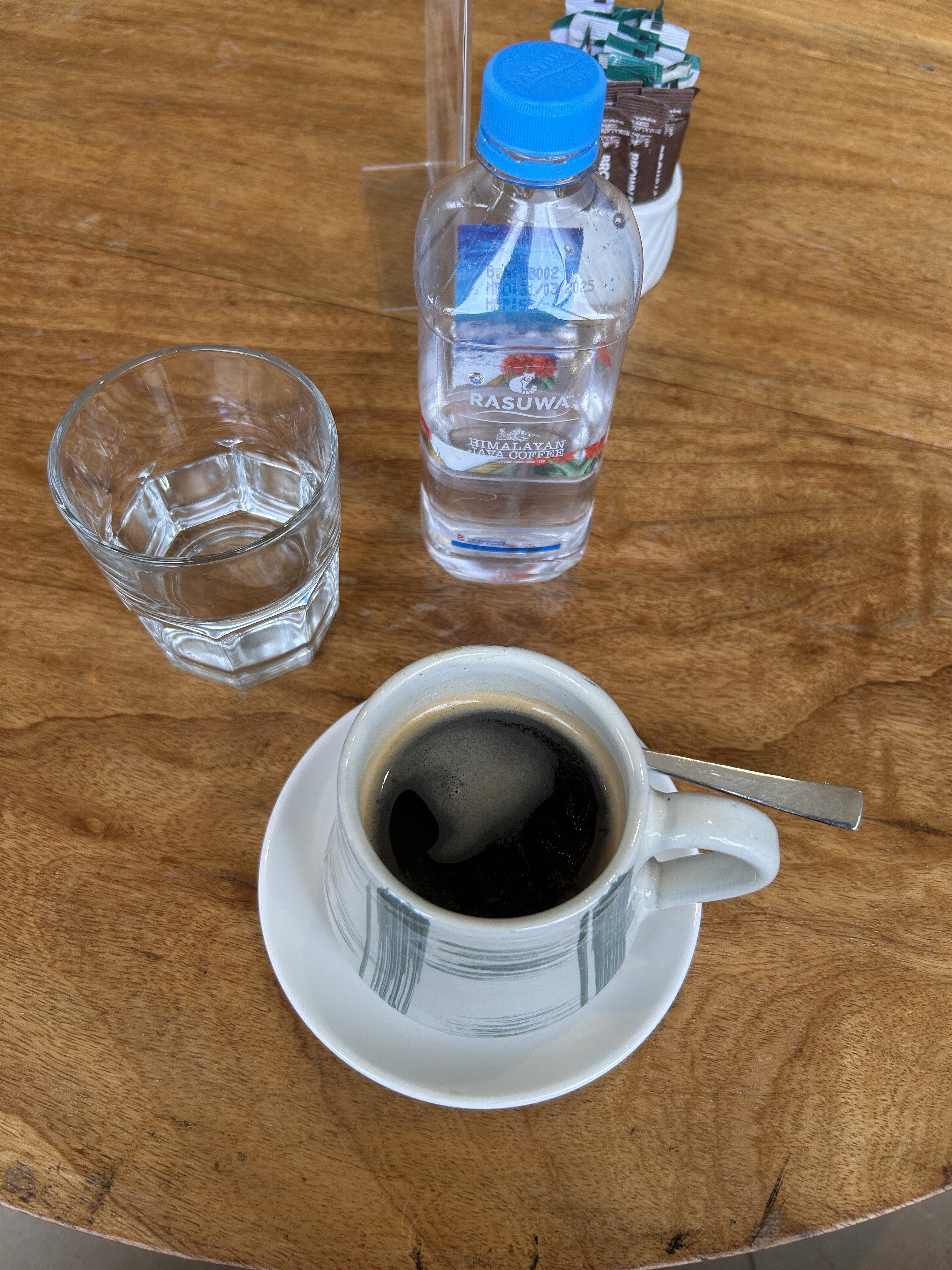 A close-up view of a wooden table featuring a cup of black coffee placed on a white saucer with a silver spoon resting on it.