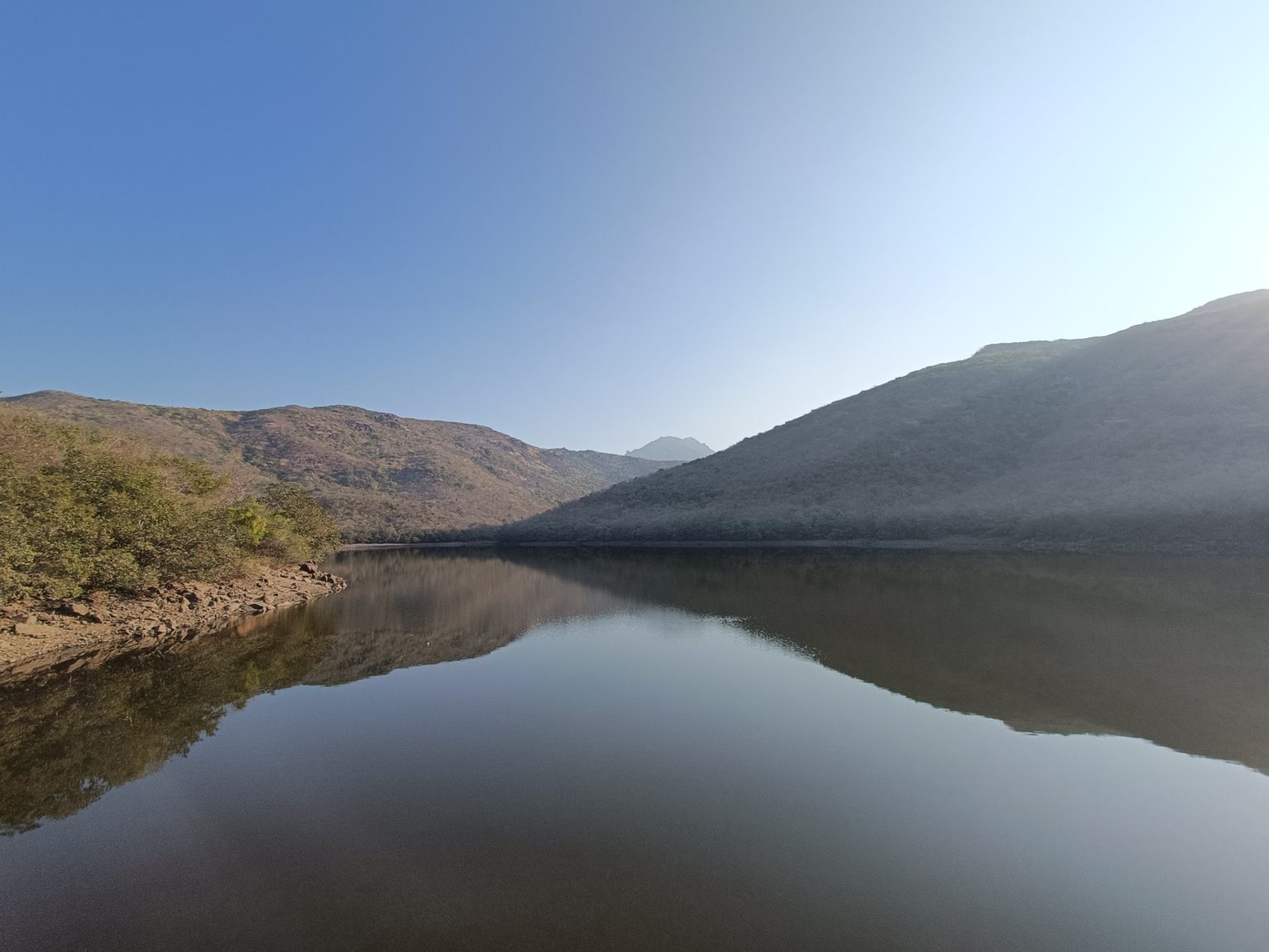 A serene landscape featuring a calm body of water reflecting the surrounding hills.