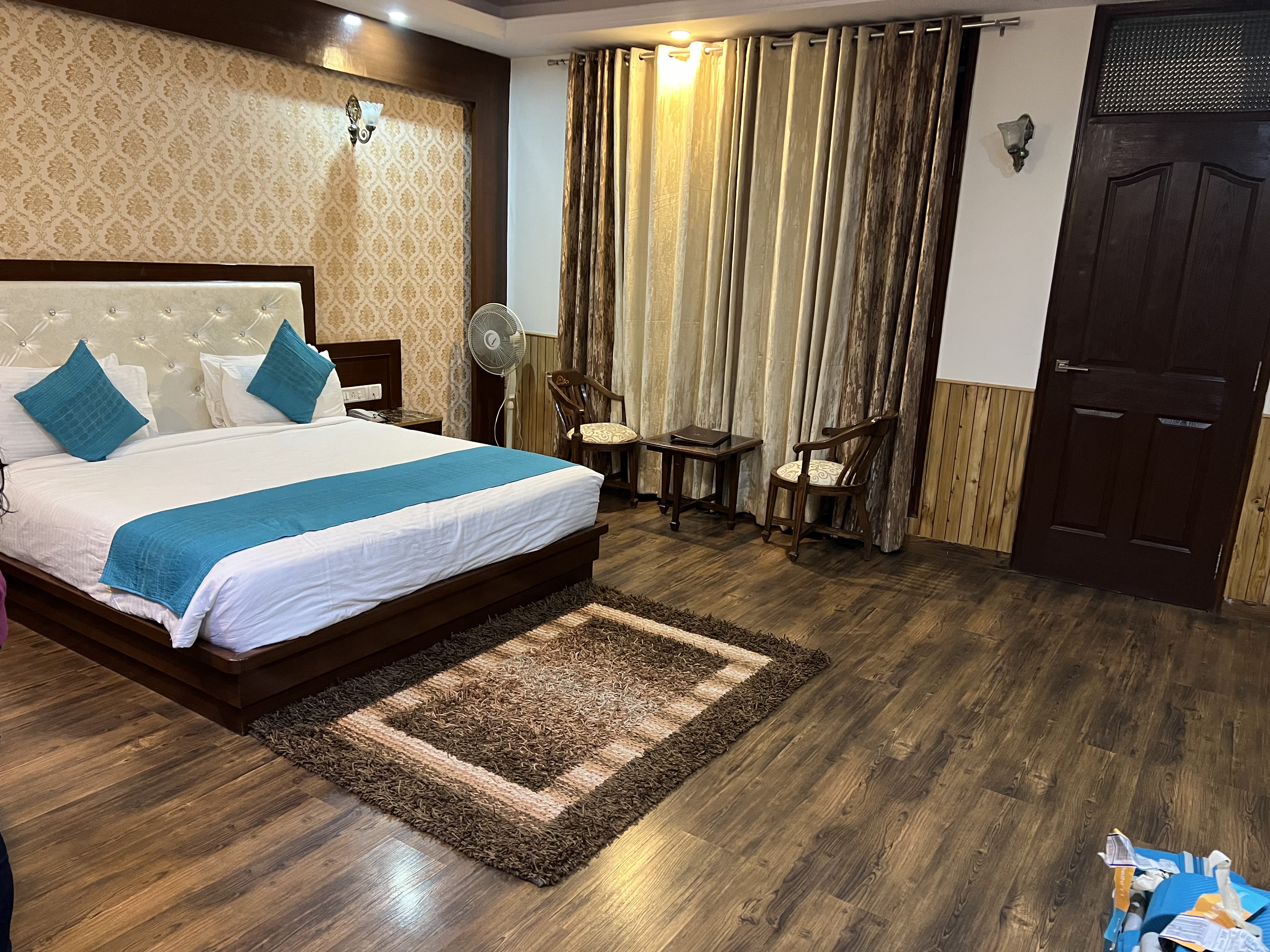A cozy hotel room featuring a queen-sized bed with a light-colored headboard and two teal cushions.
